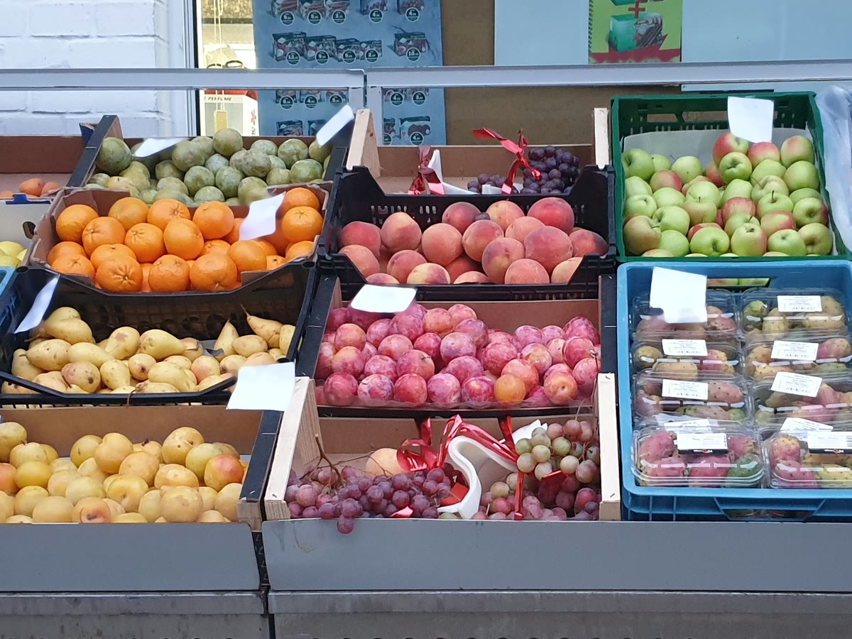 Obststand vor dem Laden: Orangen, Pfirsiche, Birnen, grüne Äpfel, Trauben und Limetten in Schalen